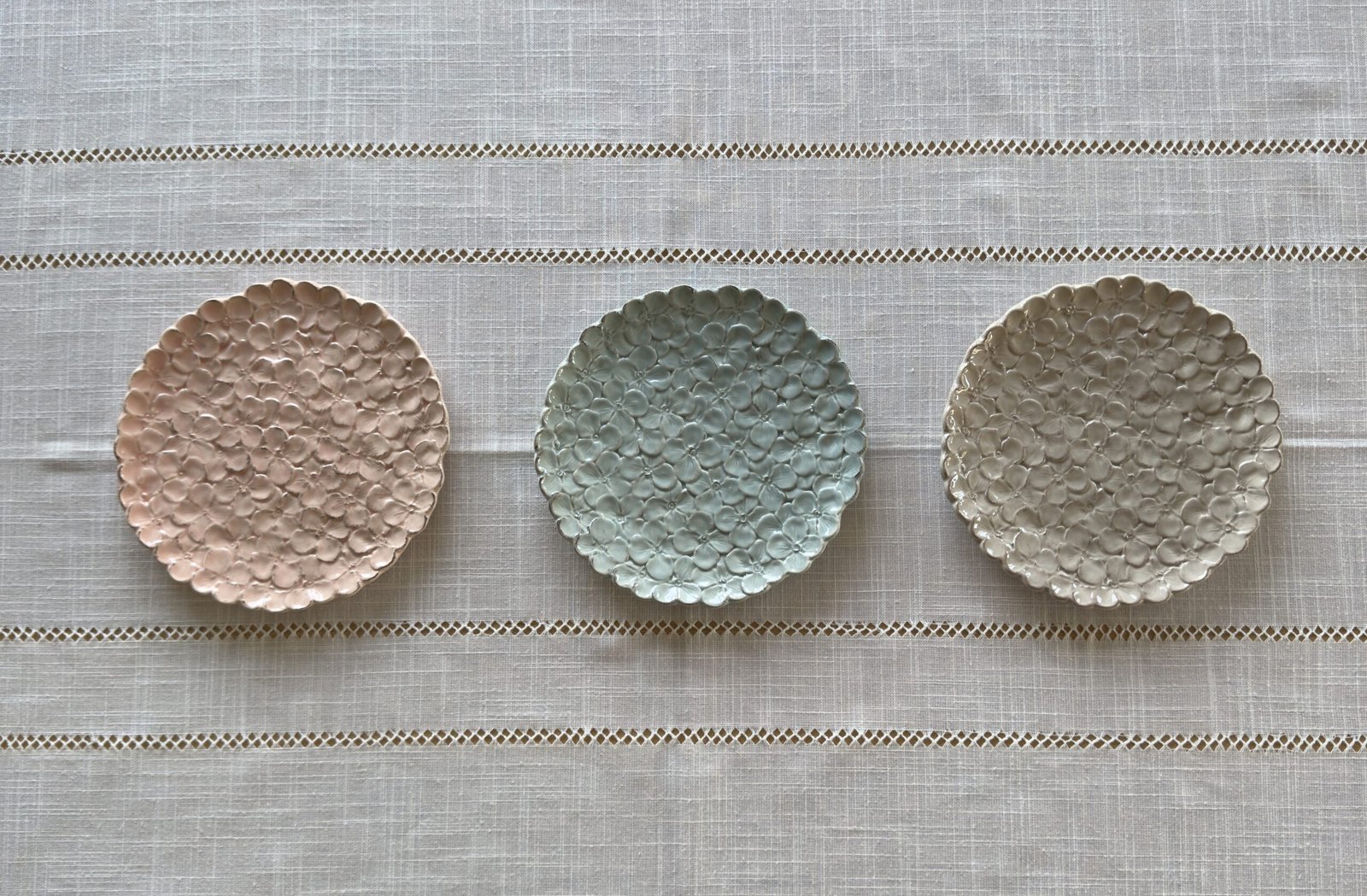 Handgemaakte keramieken ontbijtborden in de vorm van hortensia’s, in roze, turquoise en wit, op een linnen tafelkleed – Italiaans servies uit Toscane